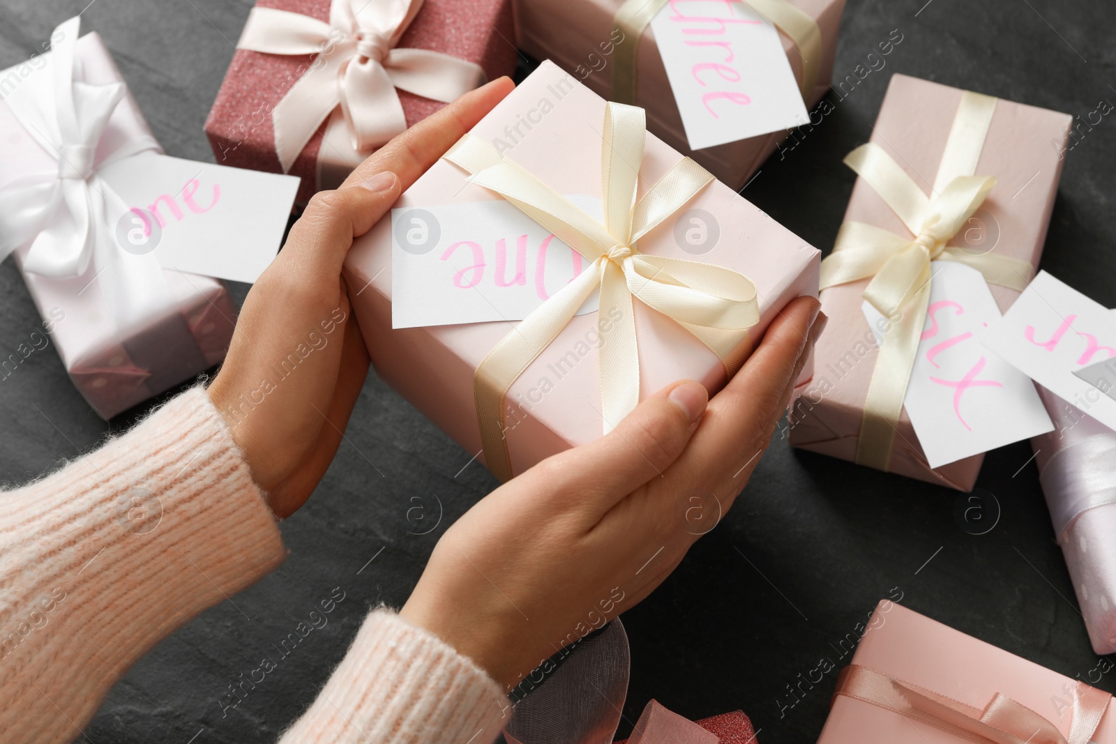 Photo of Woman with gift box at black table, closeup. Advent calendar