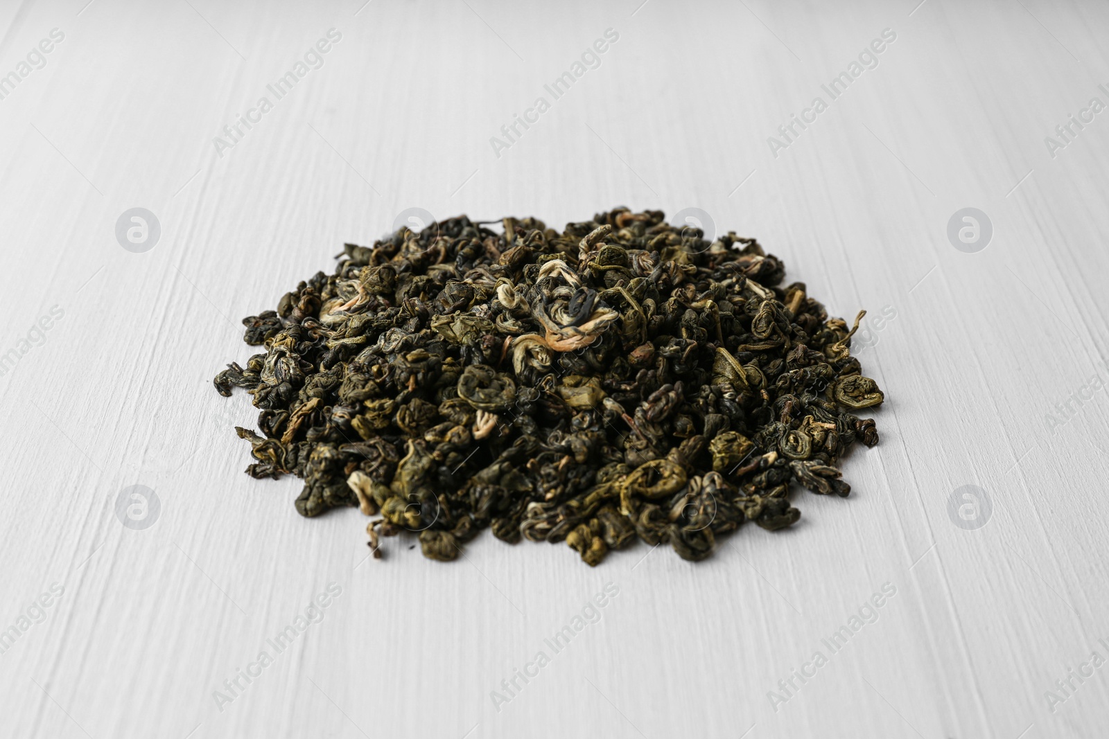 Photo of Heap of dry green tea leaves on white wooden table