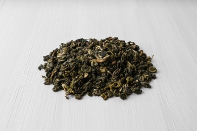 Photo of Heap of dry green tea leaves on white wooden table