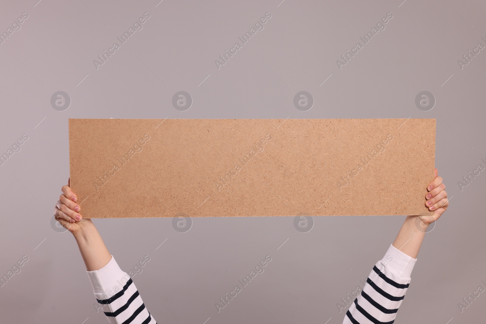 Photo of Woman holding blank cardboard banner on light grey background, closeup. Space for text