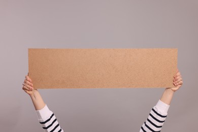 Woman holding blank cardboard banner on light grey background, closeup. Space for text