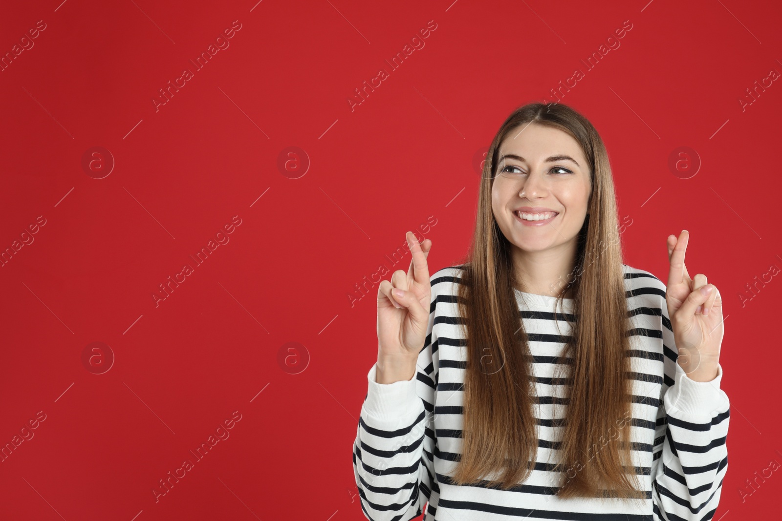 Photo of Woman with crossed fingers on red background, space for text. Superstition concept