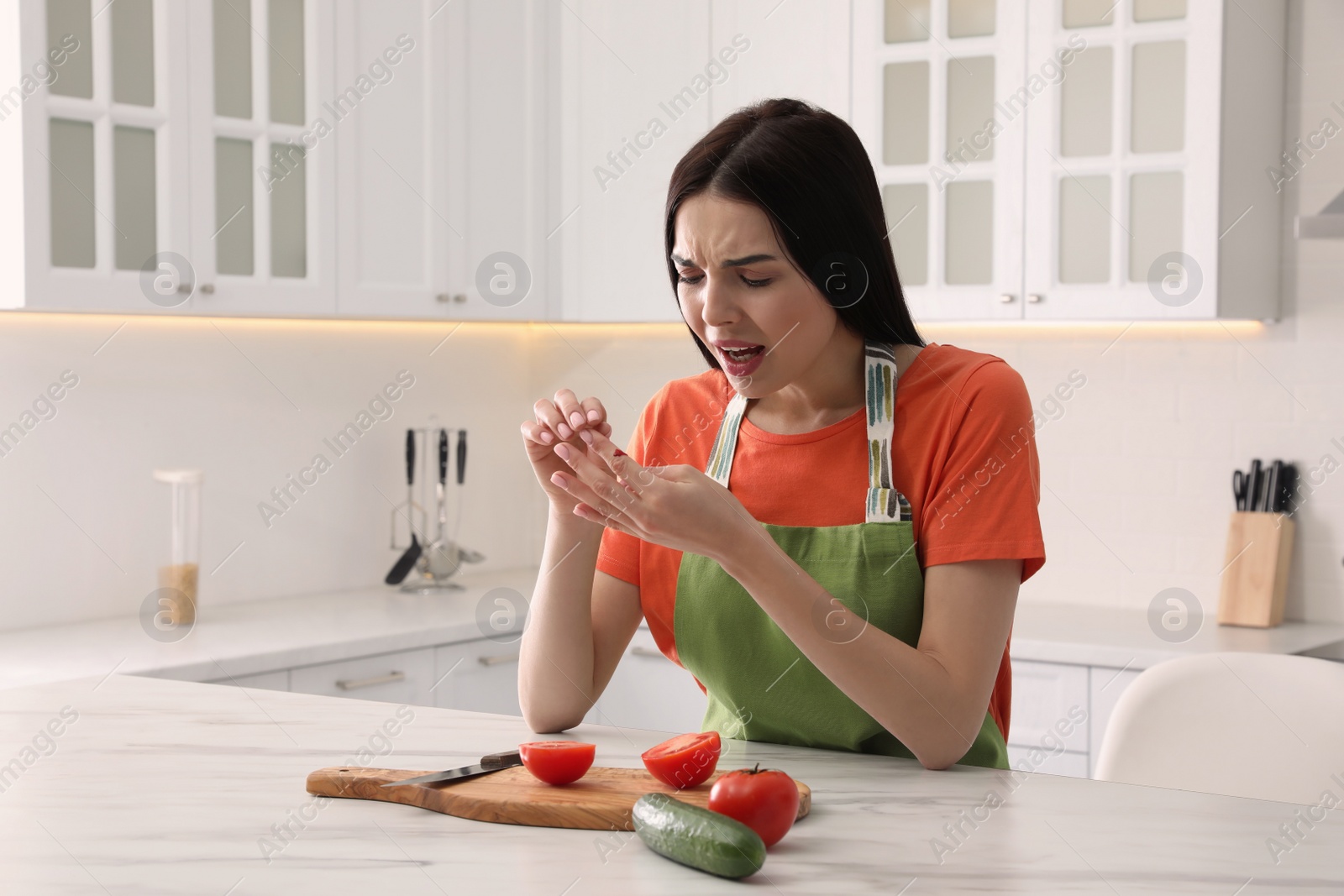 Photo of Young woman cutting finger with knife while cooking in kitchen