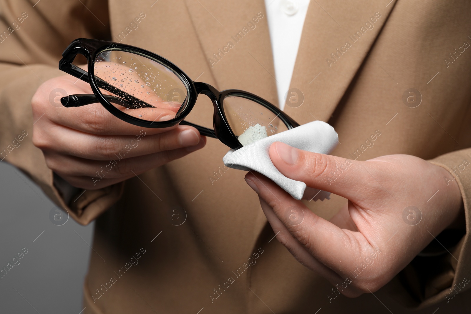 Photo of Woman wiping her glasses with microfiber cloth on grey background, closeup