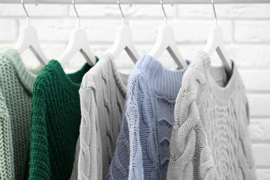 Collection of warm sweaters hanging on rack near brick wall, closeup