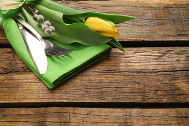 Photo of Cutlery set with beautiful willow branch and tulip on wooden table, space for text. Easter celebration