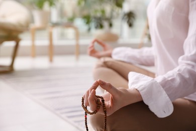 Photo of Woman with beads meditating at home, closeup. Space for text