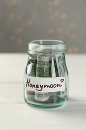 Photo of Honeymoon concept. Glass jar with dollar banknotes on white wooden table, closeup
