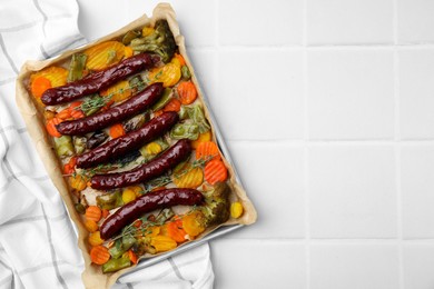 Photo of Baking tray with delicious smoked sausages and vegetables on white tiled table, top view. Space for text