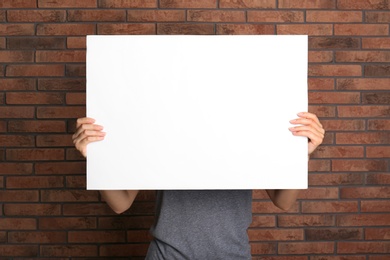Photo of Woman holding white blank poster near red brick wall. Mockup for design
