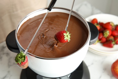 Photo of Dipping strawberry into pot with chocolate fondue on table