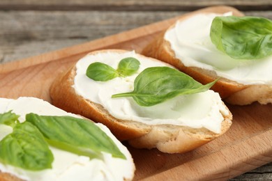 Photo of Delicious sandwiches with cream cheese and basil leaves on wooden table, closeup