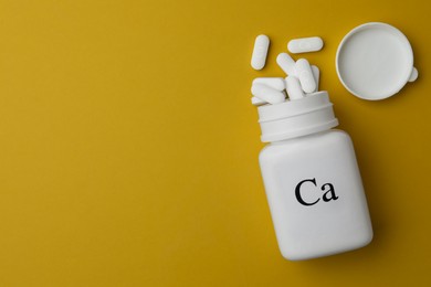 Photo of Calcium supplement pills and overturned jar on yellow background, flat lay. Space for text