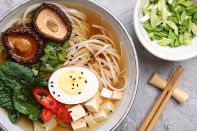 Photo of Delicious vegetarian ramen served on grey table, flat lay. Noodle soup