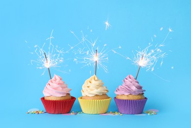 Photo of Birthday cupcakes with burning sparklers and sprinkles on light blue background