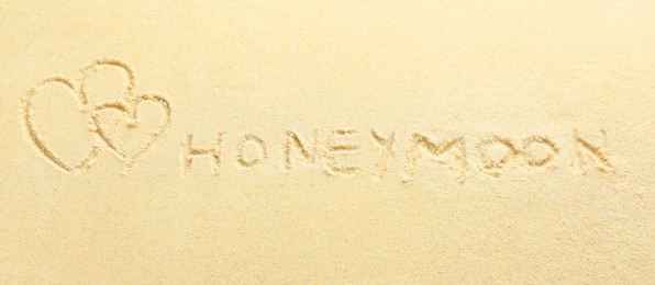 Photo of Word Honeymoon written on sand and hearts, top view