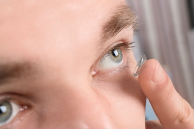Photo of Young man putting contact lens into his eye, closeup