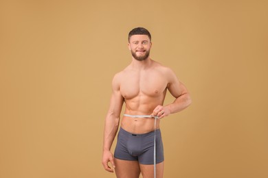 Photo of Athletic man measuring waist with tape on brown background. Weight loss concept