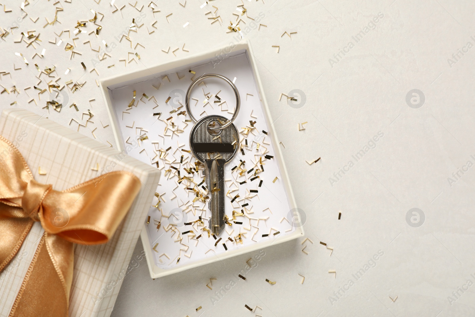 Photo of Key with confetti in gift box on white table, flat lay and space for text. Housewarming party