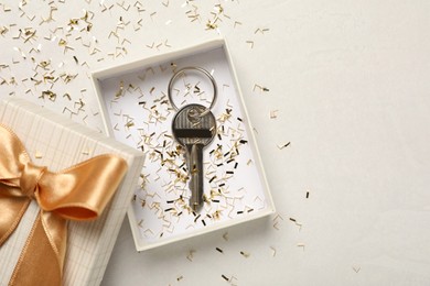 Photo of Key with confetti in gift box on white table, flat lay and space for text. Housewarming party