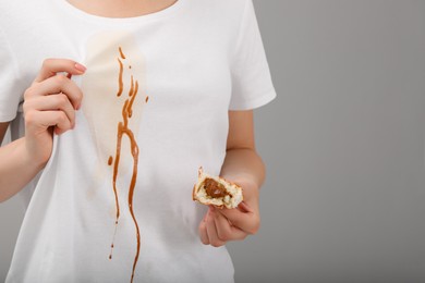 Photo of Woman holding pastry and showing stain from condensed milk on her shirt against light grey background, closeup. Space for text