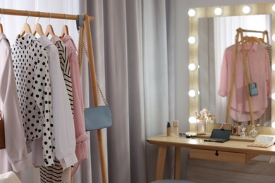 Photo of Makeup room. Clothes rack and stylish mirror with light bulbs on dressing table indoors