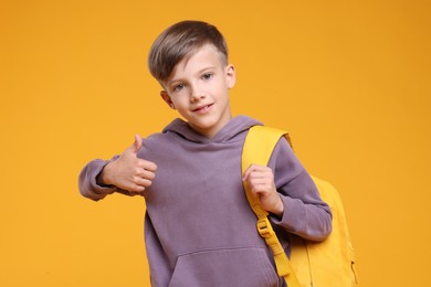 Photo of Cute schoolboy showing thumbs up on orange background