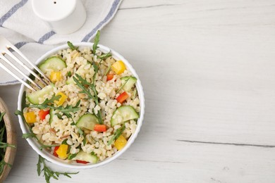 Photo of Cooked bulgur with vegetables in bowl on white wooden table, top view. Space for text