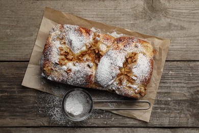 Photo of Delicious yeast dough cake and strainer with powdered sugar on wooden table, flat lay