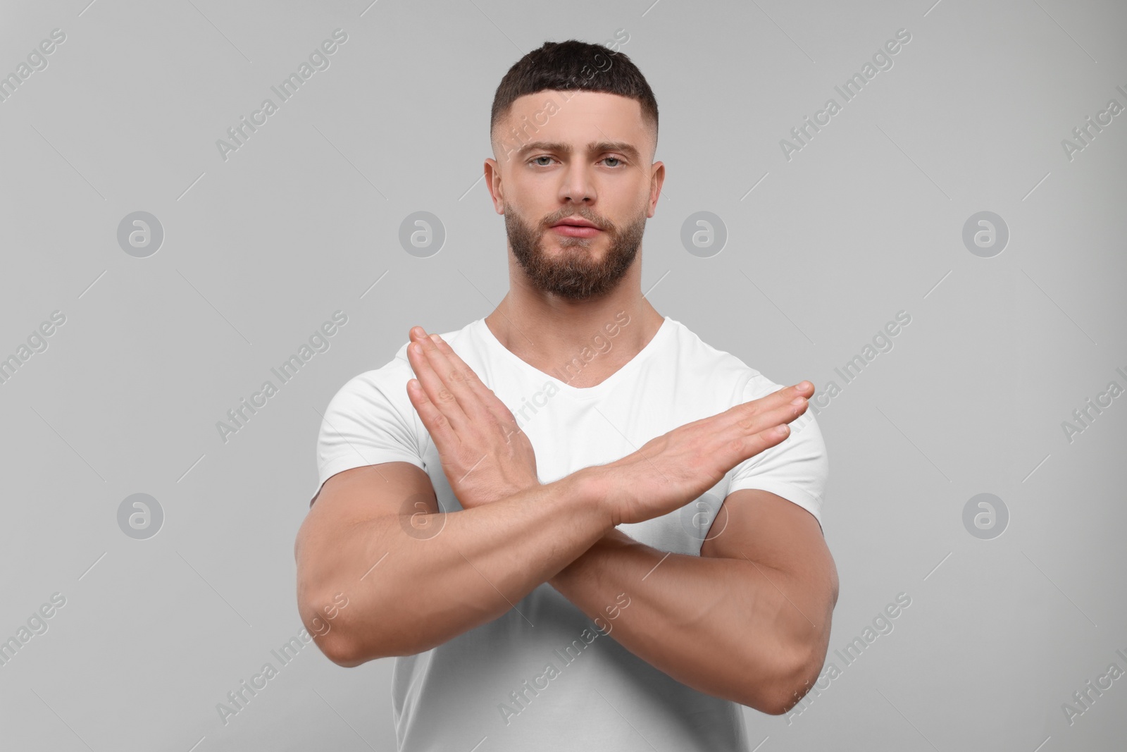 Photo of Stop gesture. Man with crossed hands on light grey background
