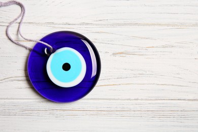 Photo of Evil eye amulet on white wooden table, top view. Space for text