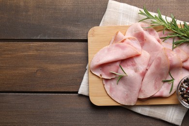 Slices of delicious ham with rosemary and spices on wooden table, top view. Space for text