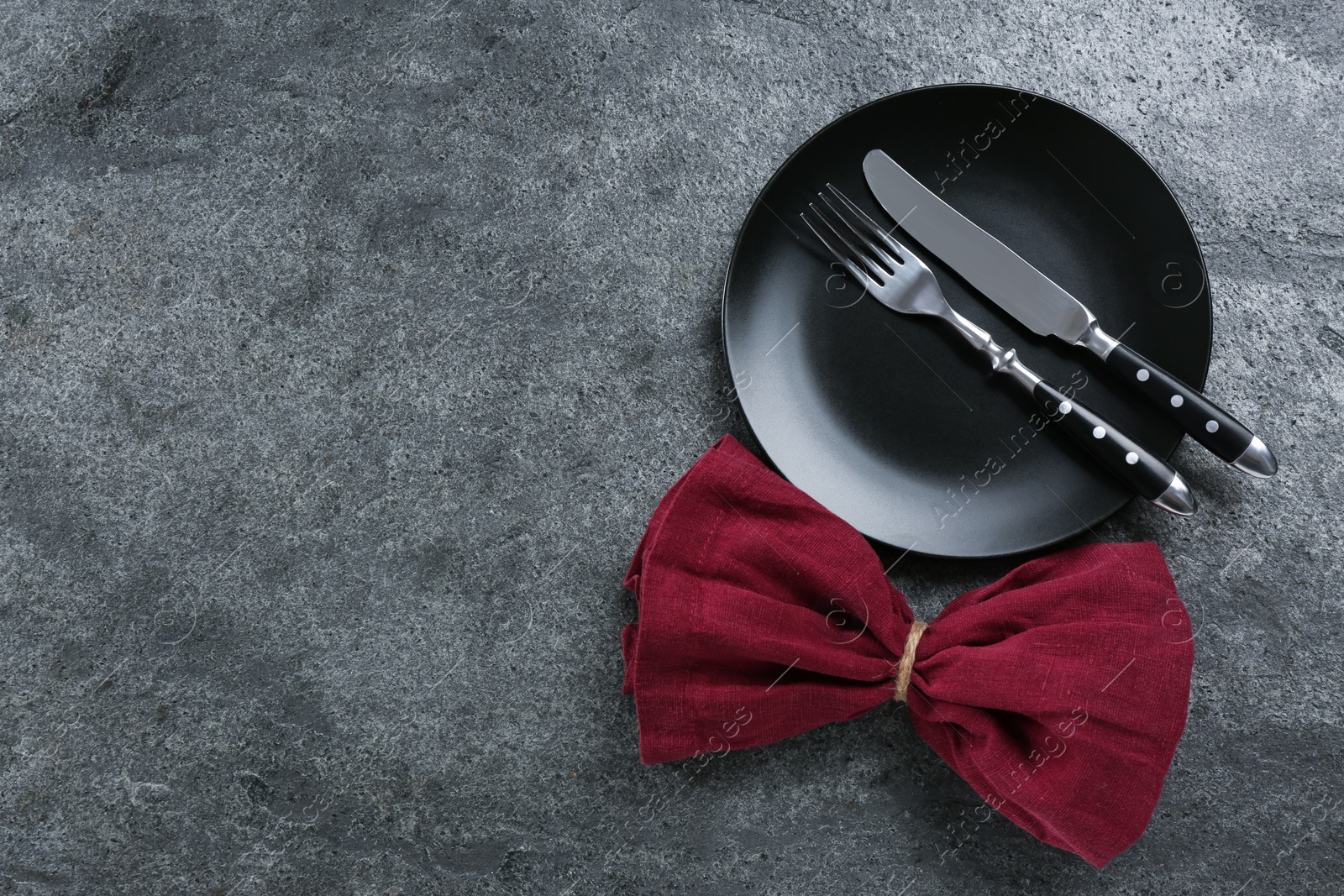 Photo of Black plate, fork, knife and napkin on grey table, flat lay. Space for text