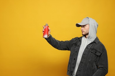 Photo of Handsome man holding can of spray paint on yellow background. Space for text