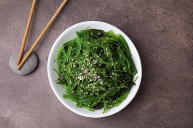 Photo of Tasty seaweed salad in bowl served on brown table, top view