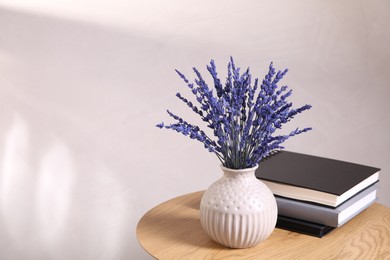 Photo of Bouquet of beautiful preserved lavender flowers and notebooks on wooden table near beige wall, space for text