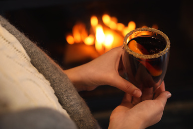 Photo of Woman with tasty mulled wine near fireplace indoors, closeup