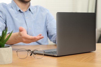 Photo of Man having video chat via laptop at wooden table indoors, closeup