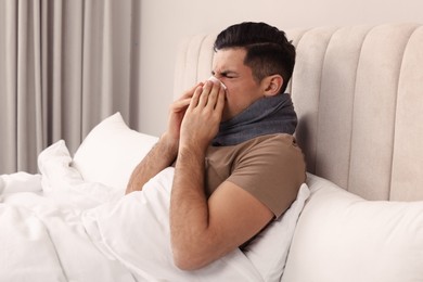 Photo of Sick man with scarf and tissue suffering from cold in bed at home