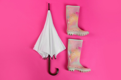 Photo of Beautiful white umbrella and colorful rubber boots on pink background, flat lay