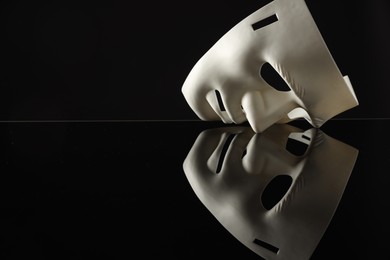 Photo of Plastic face mask on black mirror surface, space for text. Theatrical performance