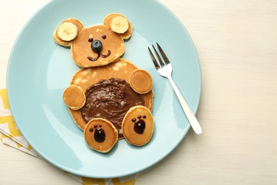 Photo of Creative serving for kids. Plate with cute bear made of pancakes, blueberries, bananas and chocolate paste on light wooden table, top view. Space for text