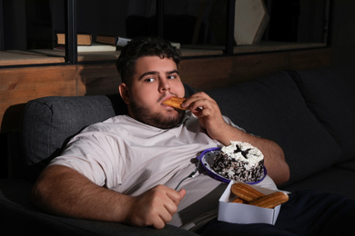 Photo of Depressed overweight man eating sweets in living room at night