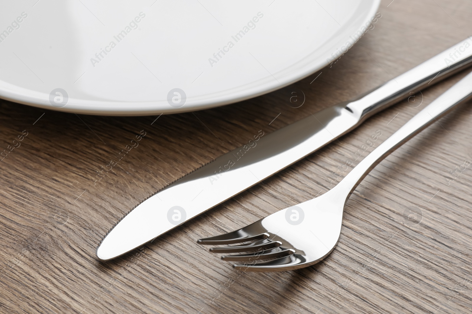 Photo of Plate, fork and knife on wooden table, closeup