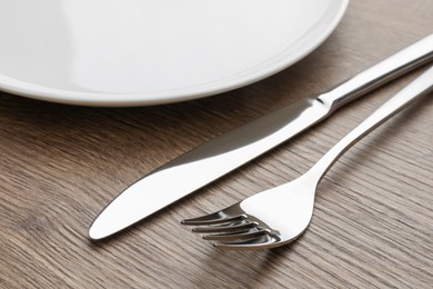Photo of Plate, fork and knife on wooden table, closeup