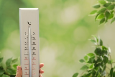 Photo of Woman with weather thermometer on blurred background, closeup. Space for text