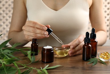 Photo of Woman dripping THC tincture or CBD oil into bowl at wooden table, closeup