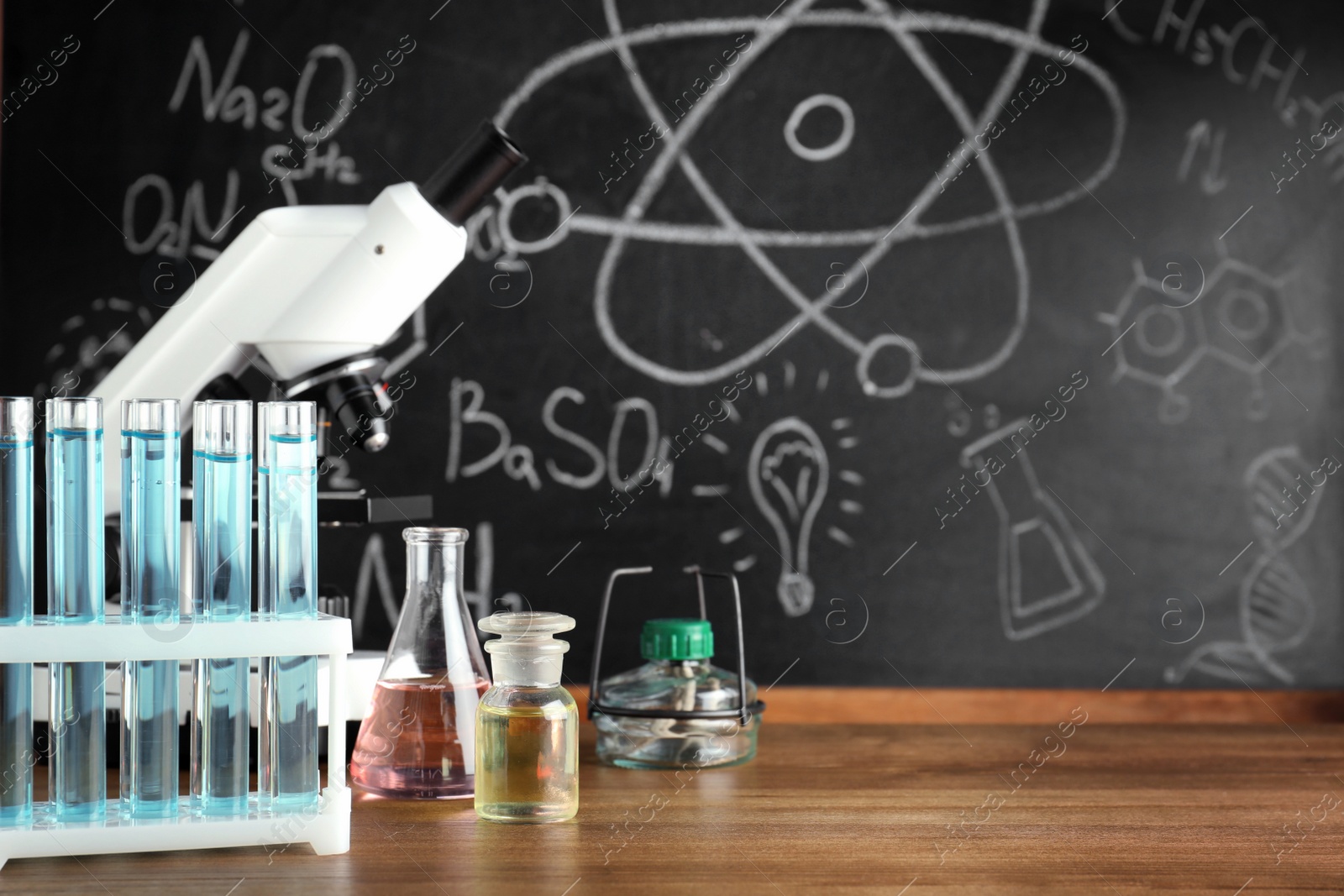 Photo of Laboratory glassware and microscope on table near chalkboard. Chemistry concept