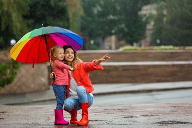 Photo of Happy mother and daughter with bright umbrella under rain outdoors