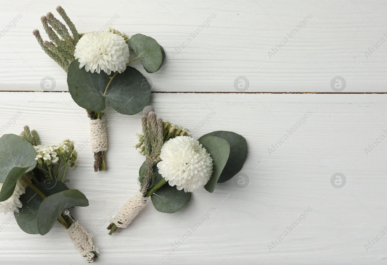 Photo of Small stylish boutonnieres on white wooden table, flat lay. Space for text